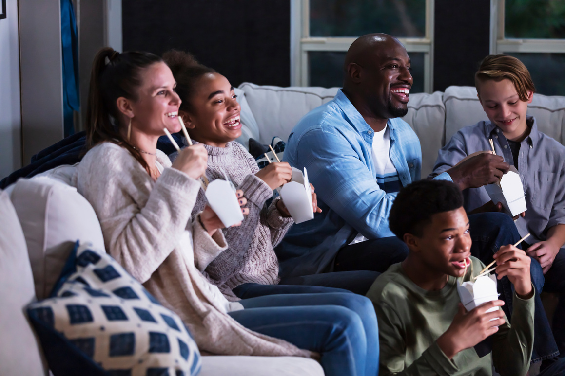 Blended family of five watching TV, eating takeout